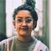 headshot of brown woman with top bun wearing round glasses and grey sweater