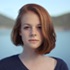 headshot of white woman with chin-length red hair with lake and mountain background