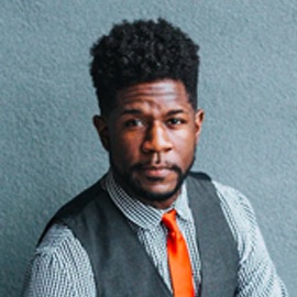 headshot of black man wearing vest and orange tie