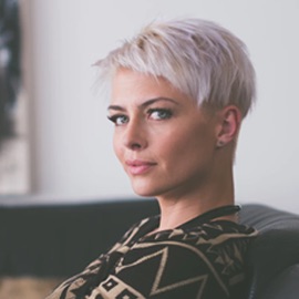 headshot of white woman with short silver hair wearing black and gold sweater